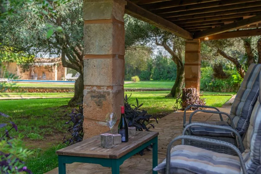 Una zona de estar al aire libre, bajo un patio cubierto, da a un jardín y una piscina.