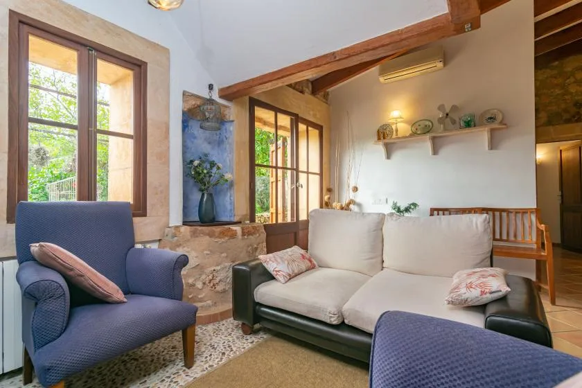 Una sala de estar con asientos acolchados, vigas de madera vistas y ventanas con vistas a la vegetación.