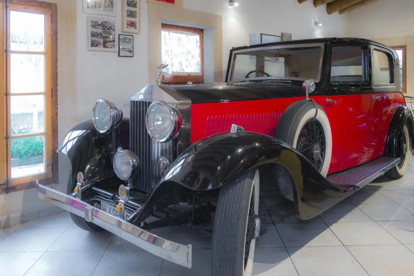 Un automóvil antiguo rojo y negro está expuesto en un interior con suelo de baldosas.