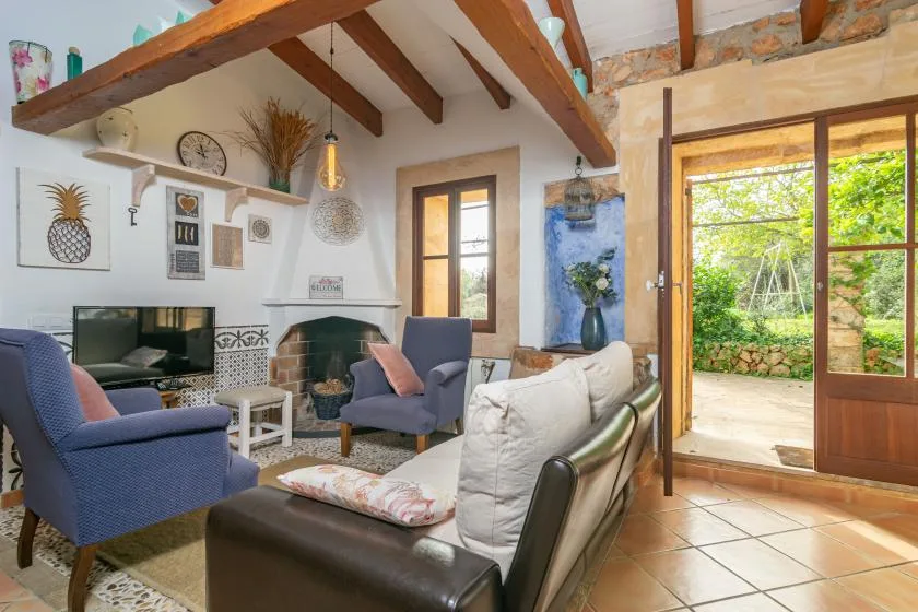 Una sala de estar con vigas de madera vistas, asientos y una puerta abierta al jardín.
