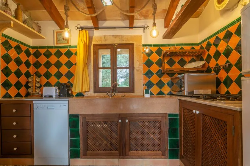 Una cocina con una ventana sobre la encimera y paredes de azulejos de colores.