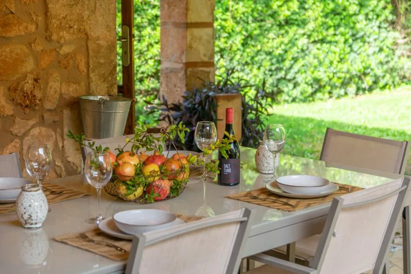 Una mesa de comedor al aire libre está puesta con platos, copas y un frutero.