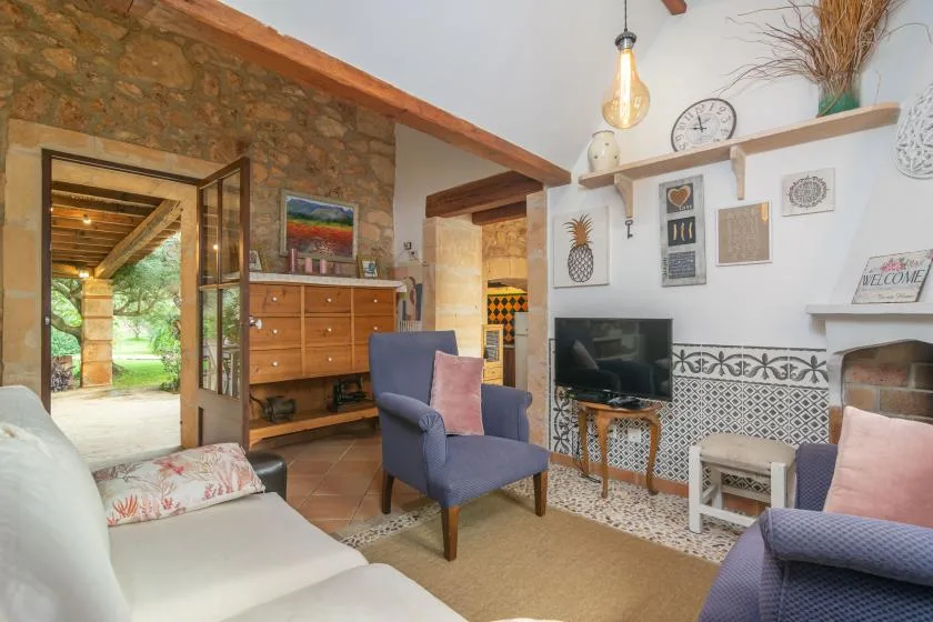 Una sala de estar con asientos, un televisor y una puerta abierta a un pasillo con paredes de piedra.