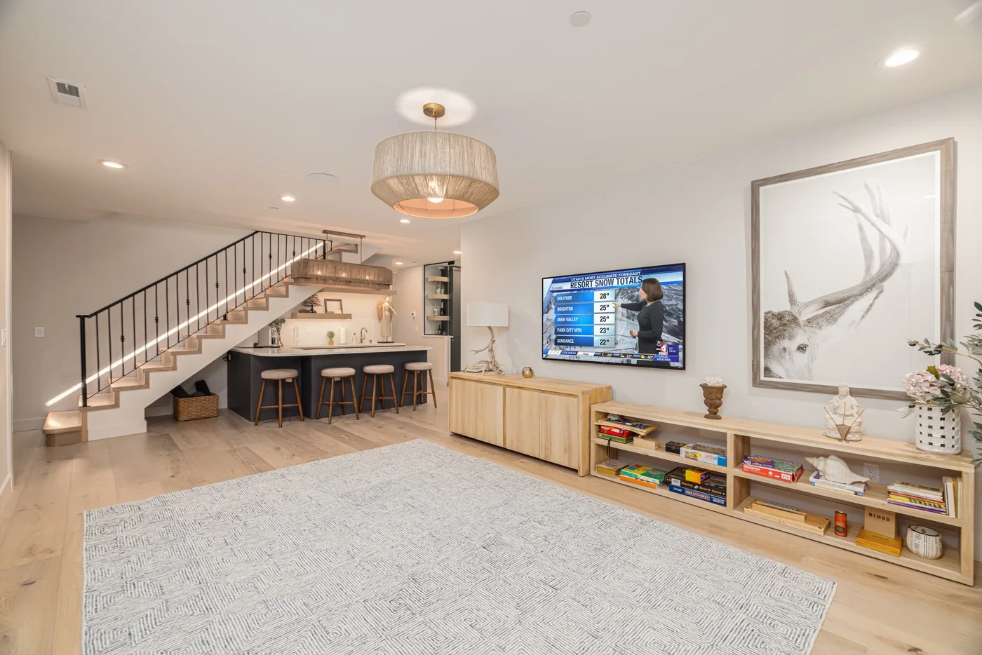 Una sala luminosa con una alfombra grande, televisor y escalera abierta.