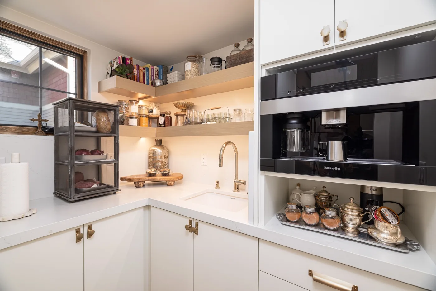 Un rincón de cocina luminoso con gabinetes blancos, estantes abiertos y electrodomésticos.