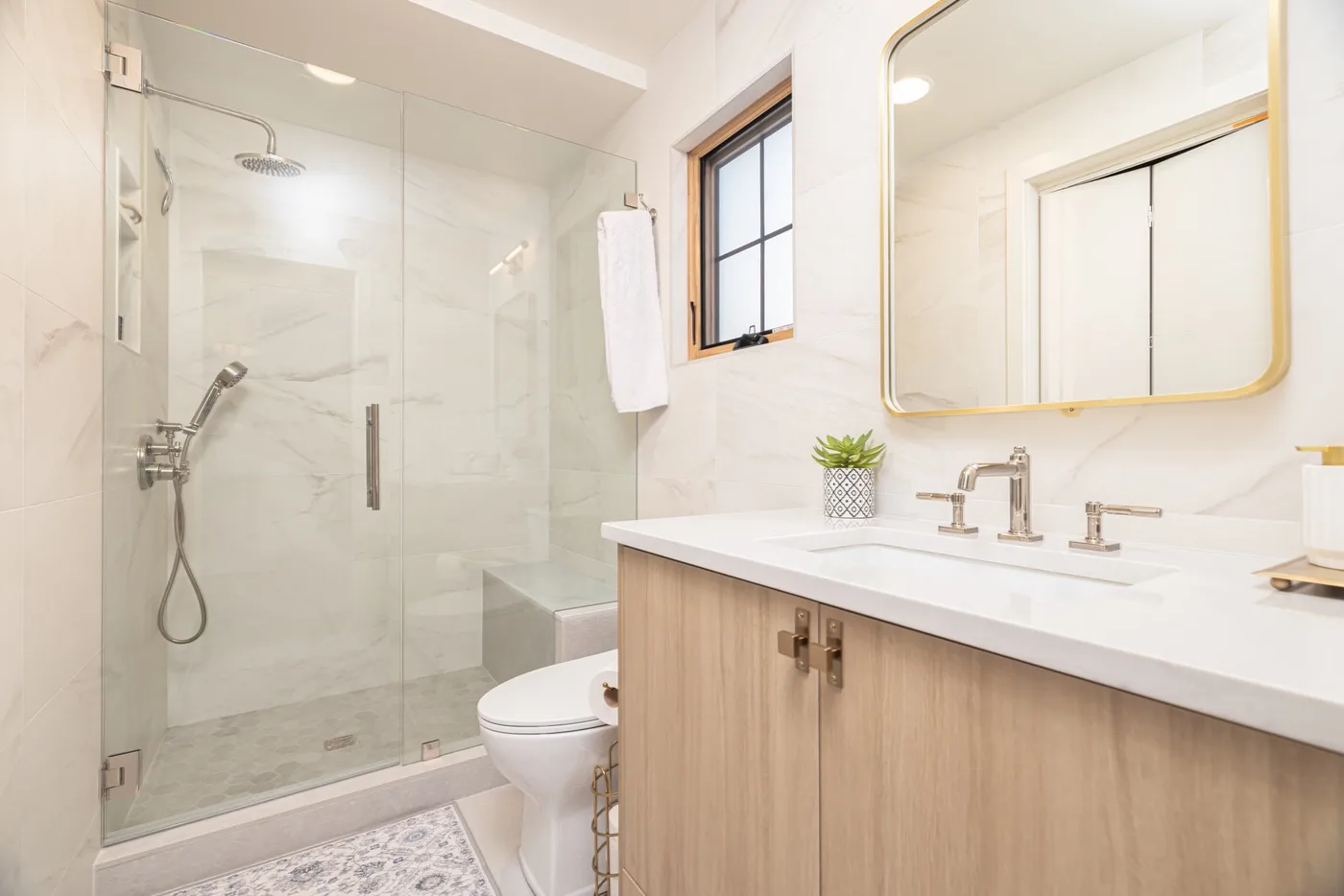 Un baño luminoso con ducha de vidrio, inodoro y tocador de madera.