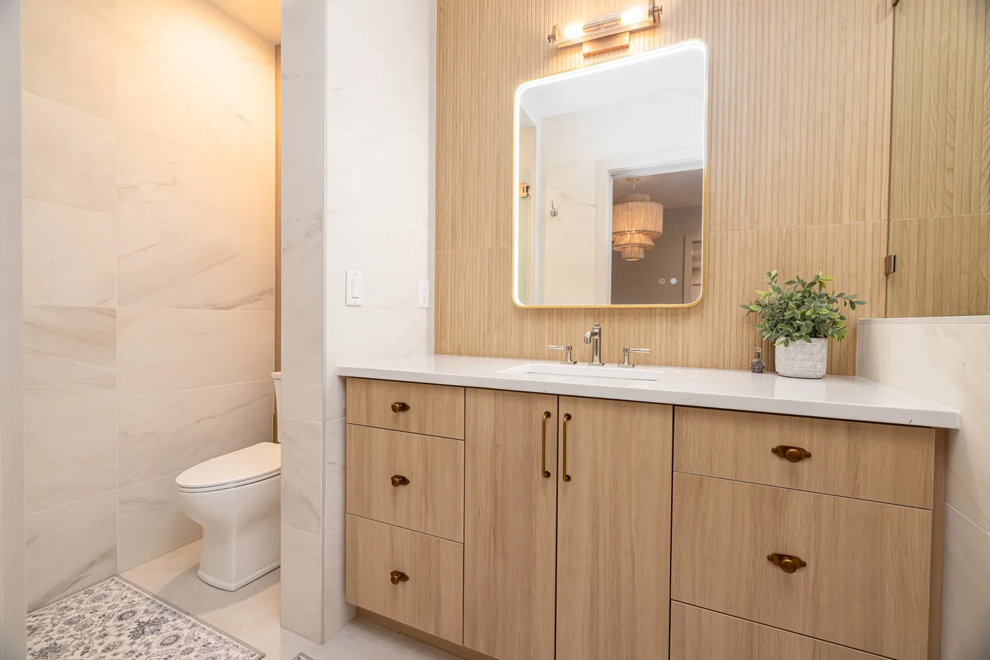 Un tocador de baño con un espejo iluminado y un inodoro al lado.