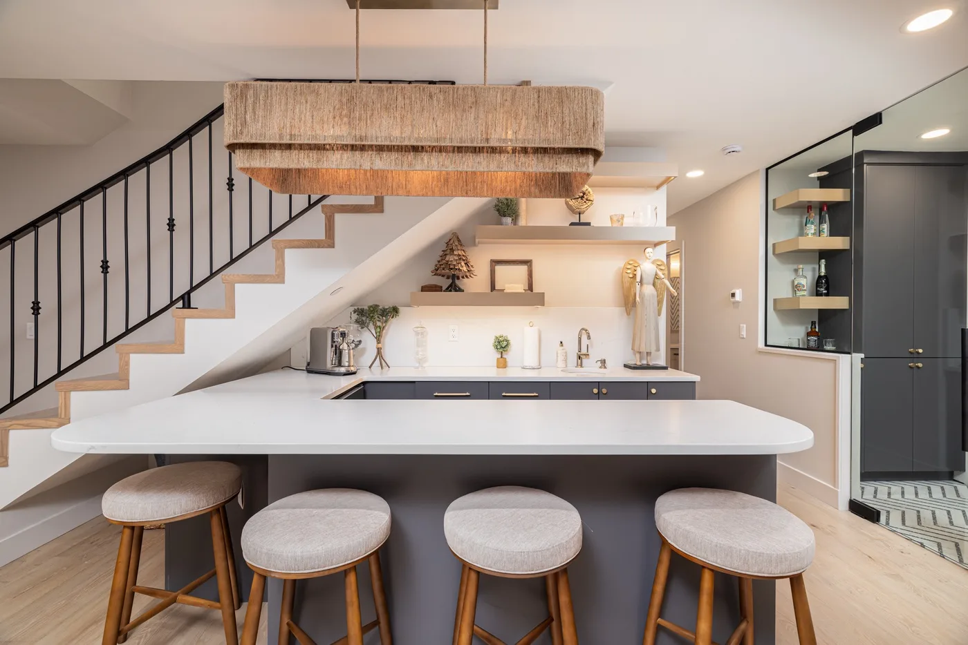 Una cocina moderna con una isla larga y taburetes bajo una escalera.