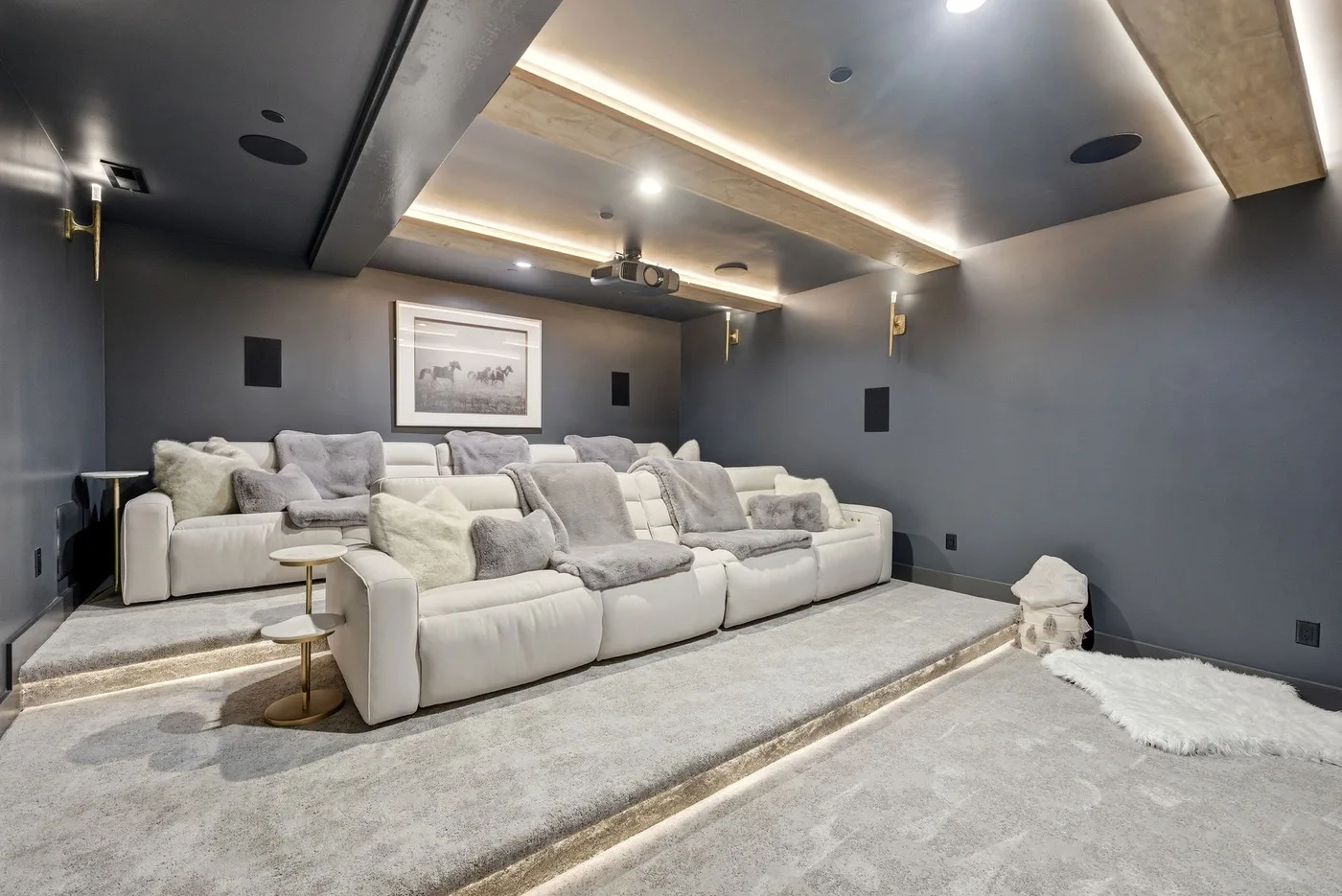 Una sala de cine en casa con filas de asientos reclinables claros y una pantalla en la pared.