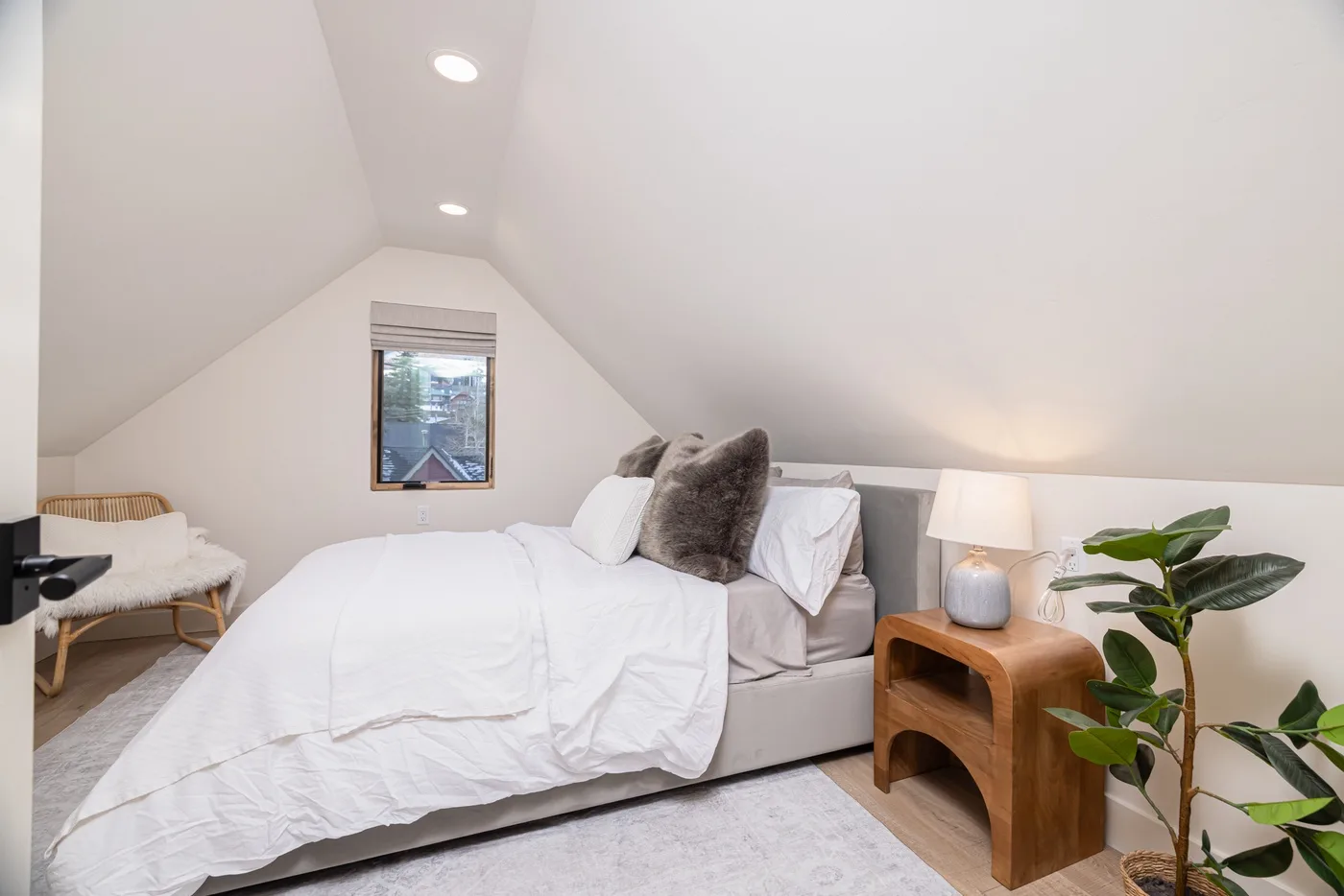 Un dormitorio abuhardillado luminoso con una cama tendida y una ventana pequeña.