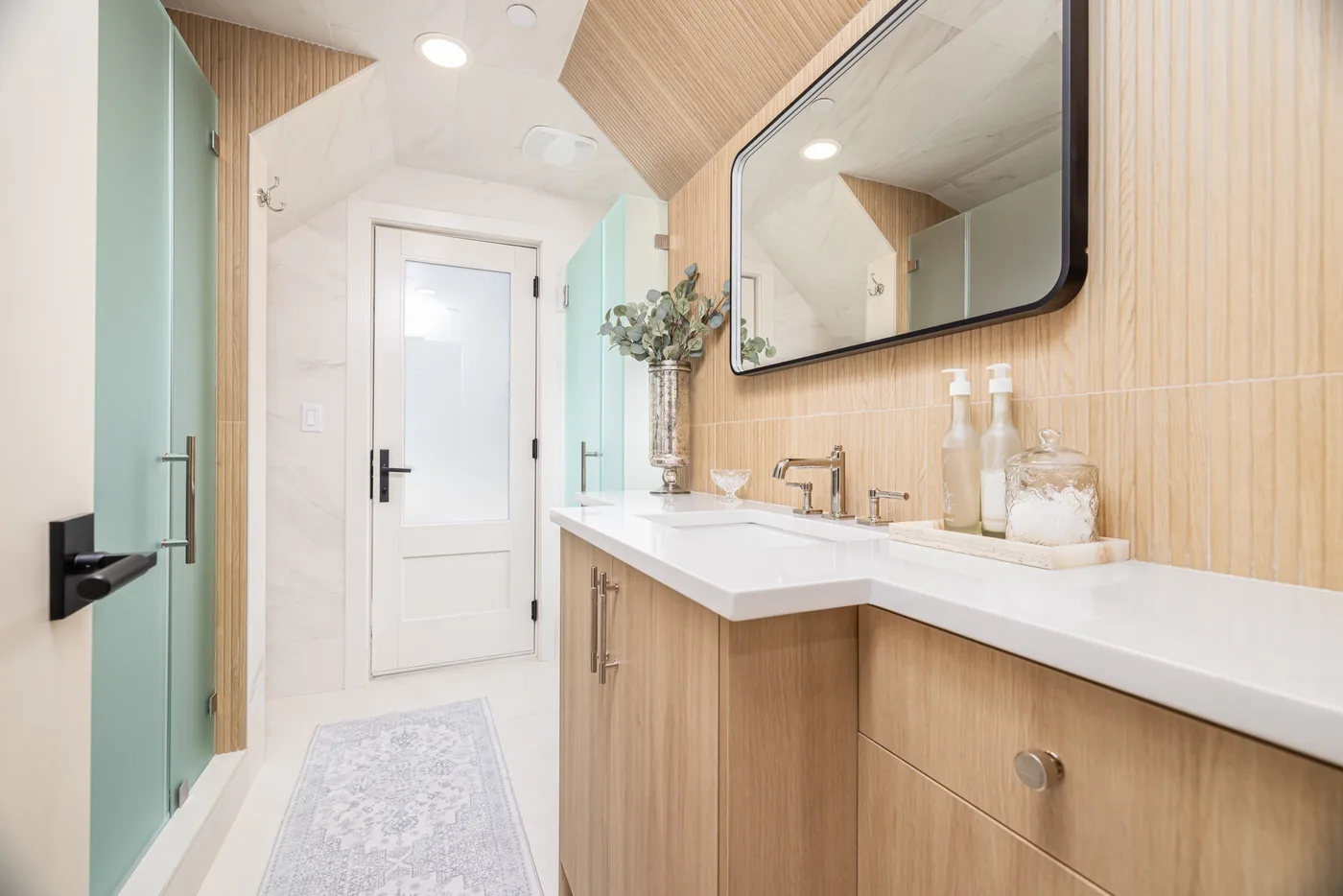 Un baño luminoso con un tocador largo, lavabo y un gran espejo de pared.