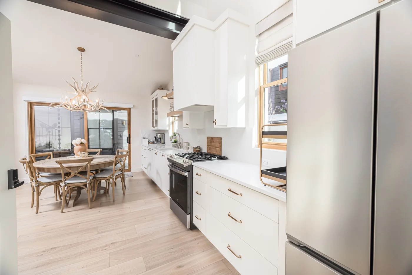 Una cocina luminosa con gabinetes blancos da a un comedor con una mesa de madera.