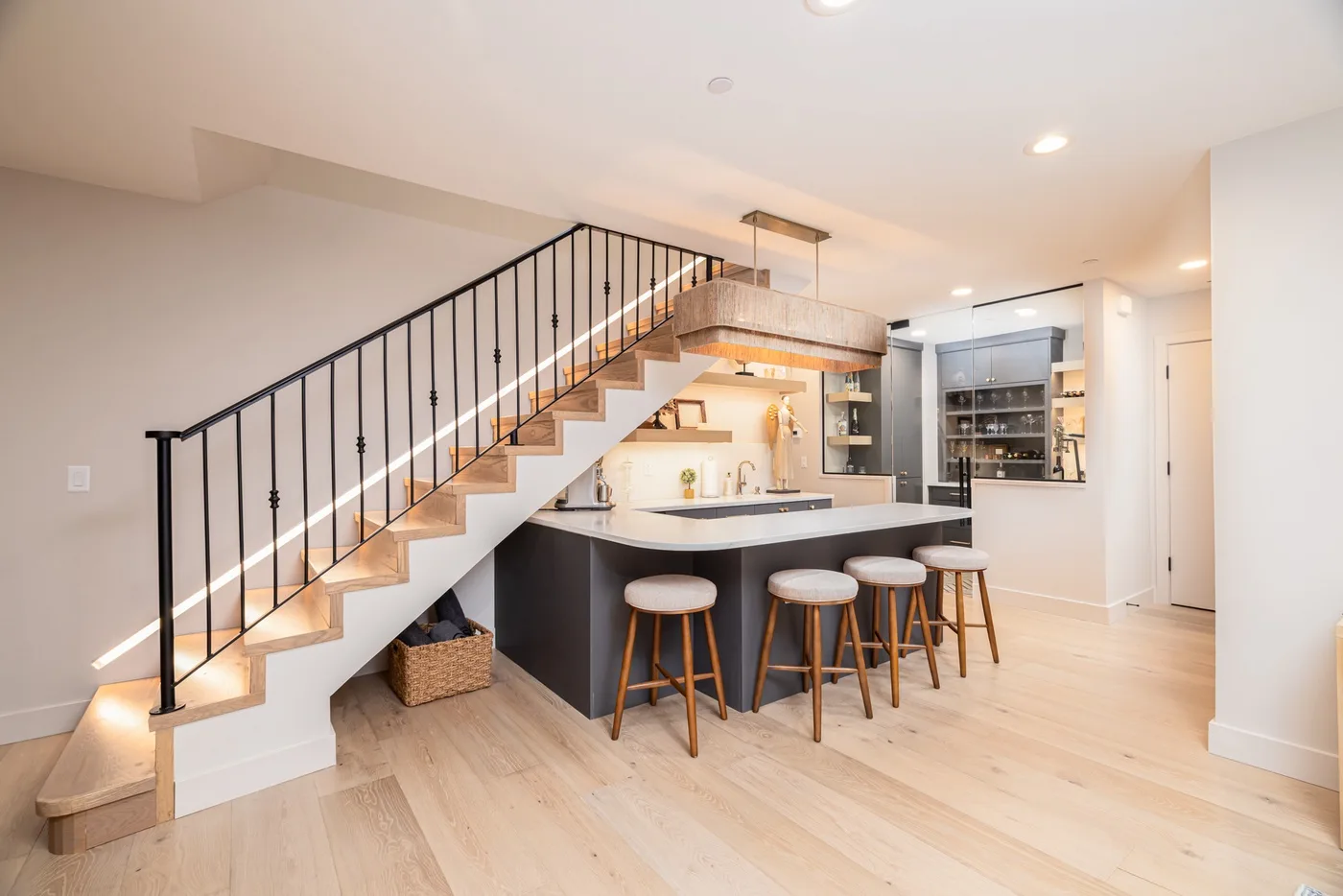 A bright kitchen and bar sit beneath a staircase with dark railings.