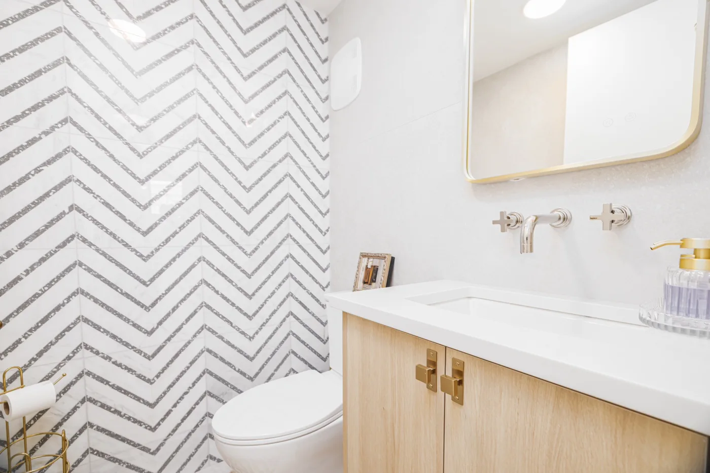 Un baño luminoso con lavabo blanco, mueble de madera y azulejos estampados.