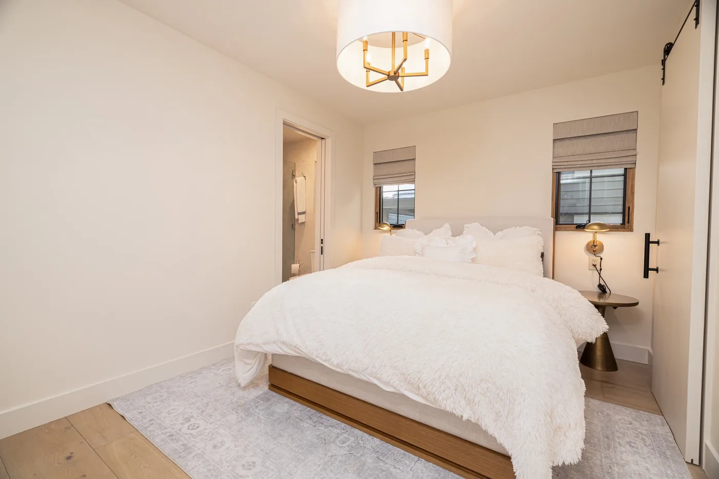Un dormitorio con una cama grande, ropa de cama blanca y dos ventanas.