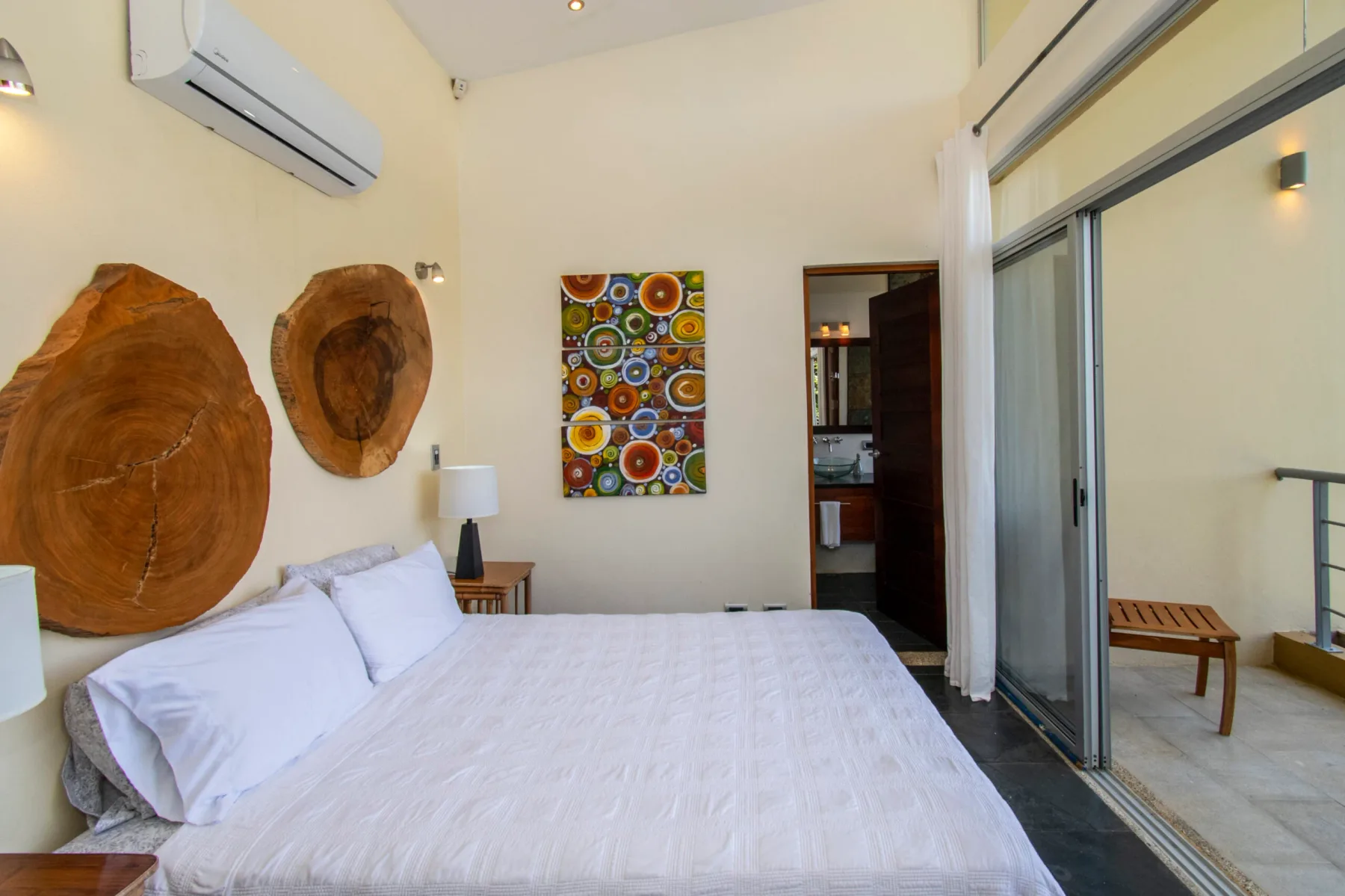 Dormitorio con una cama tendida y una colorida obra de arte en la pared.