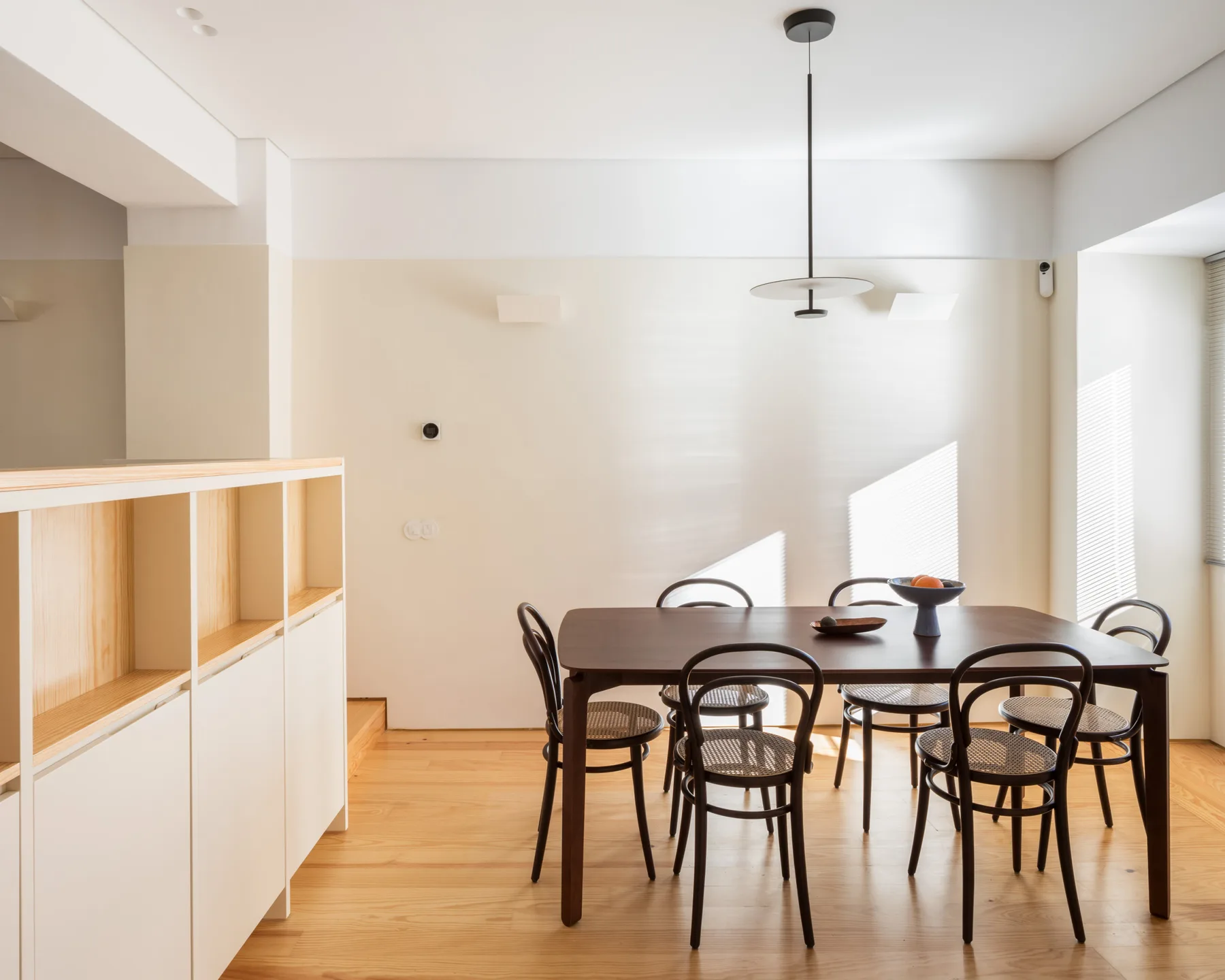 Un comedor luminoso tiene una mesa larga y asientos oscuros.