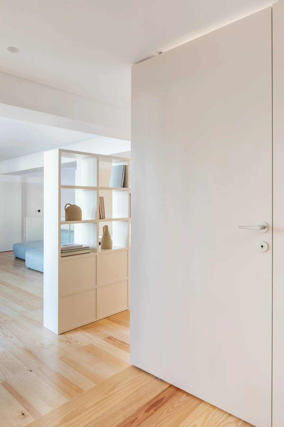 An open doorway leads into a bright room with light wood flooring and shelving.