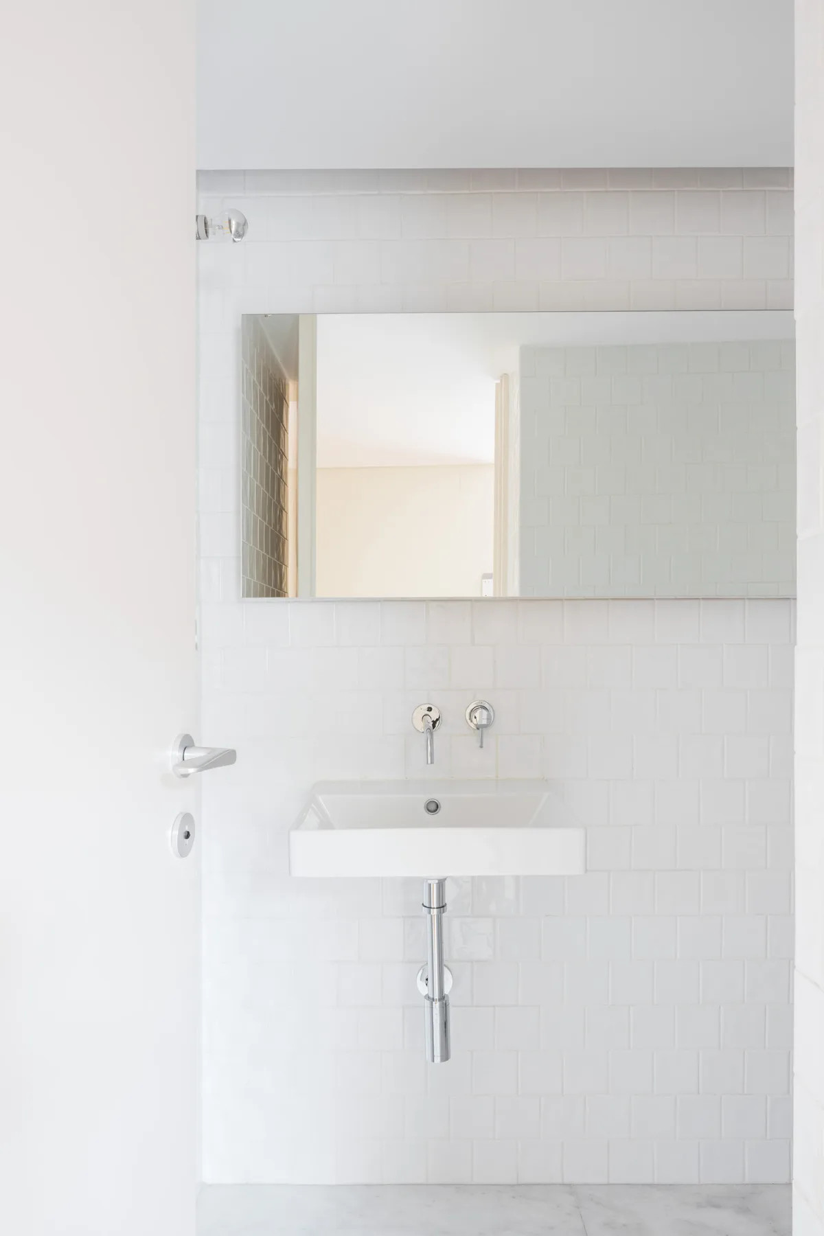 A bright bathroom with a wall-mounted sink and large mirror.