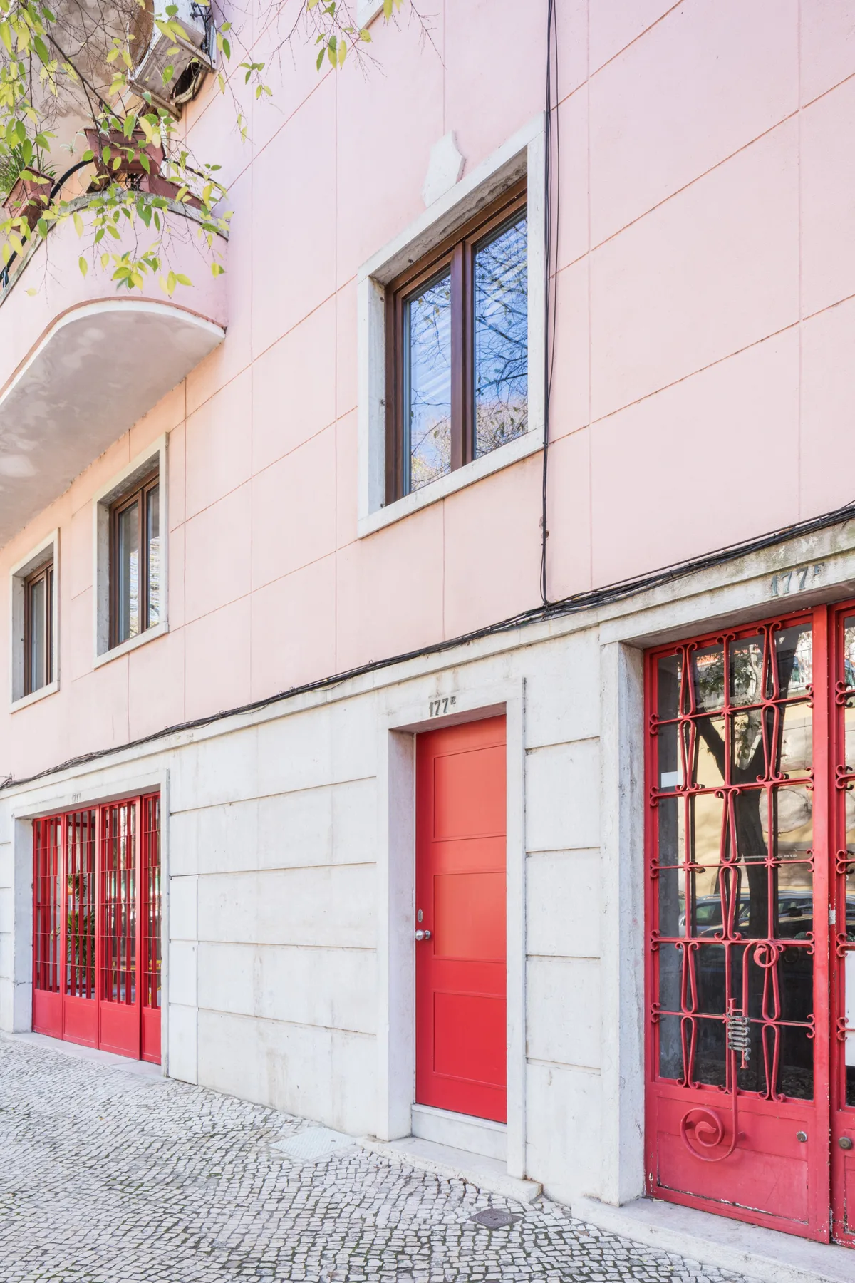 A pink street-facing building with a red entrance door and barred windows.