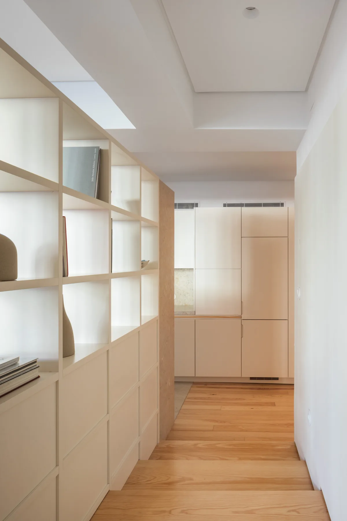 Un pasillo luminoso con estanterías empotradas y suelo de madera clara.