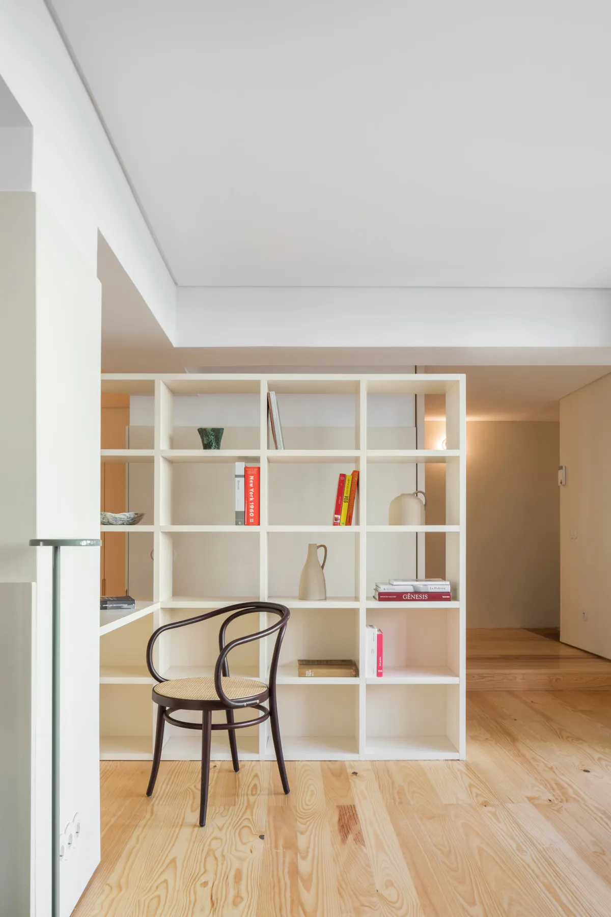 Una sala luminosa con una estantería divisoria y una silla sobre un suelo de madera.