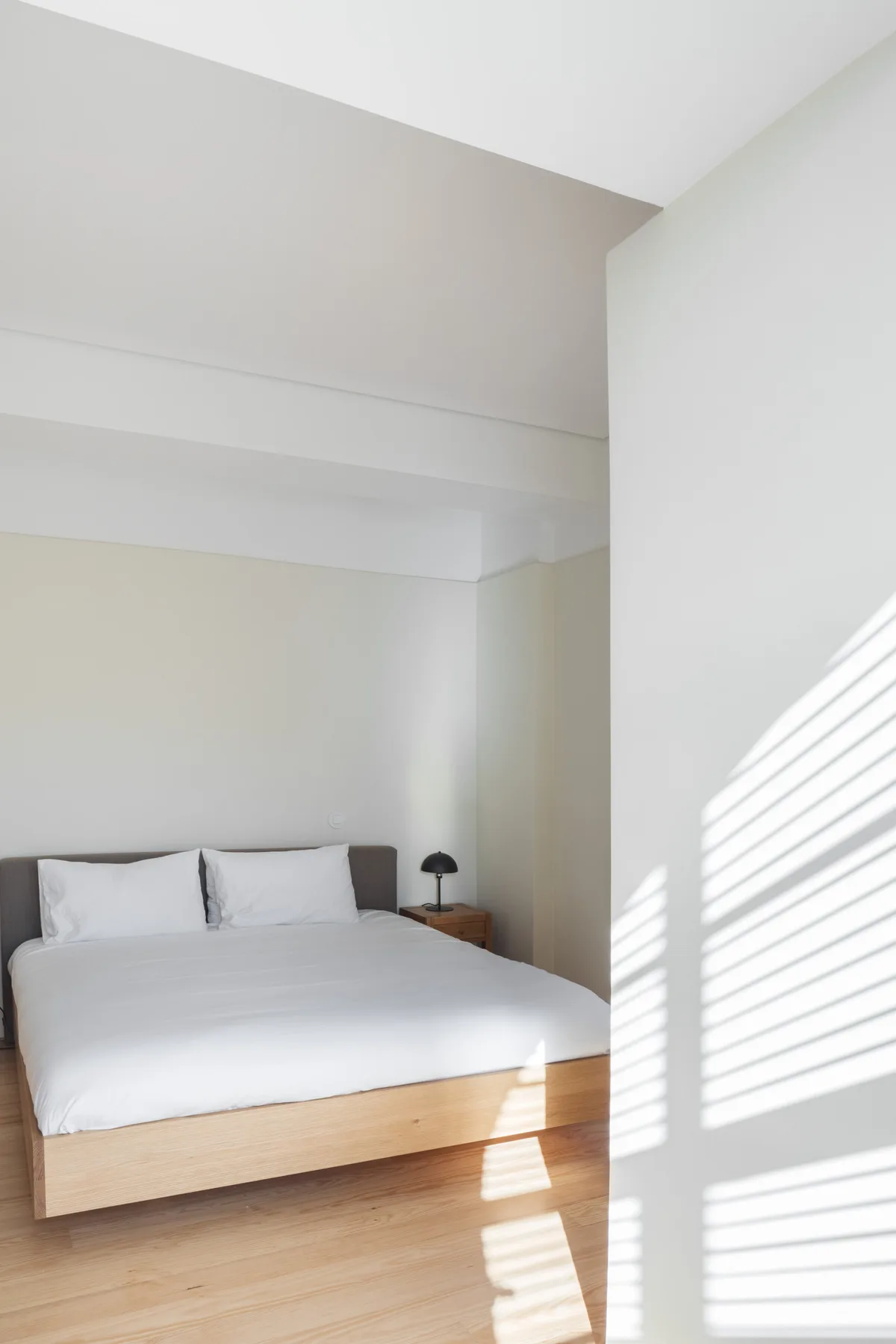 A bright bedroom with a neatly made bed and sunlight across the floor.