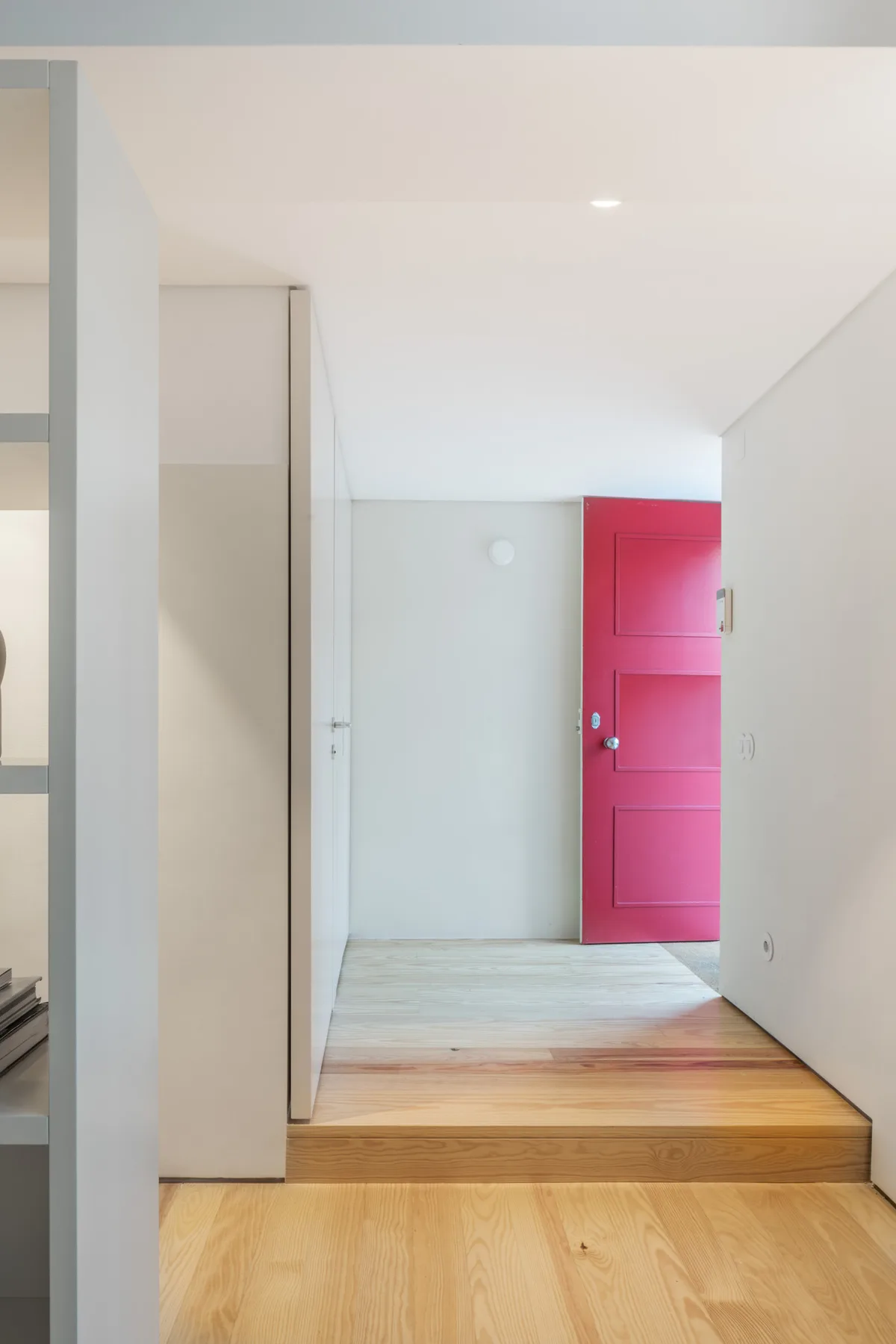 A bright interior hallway leads to a vivid pink door.