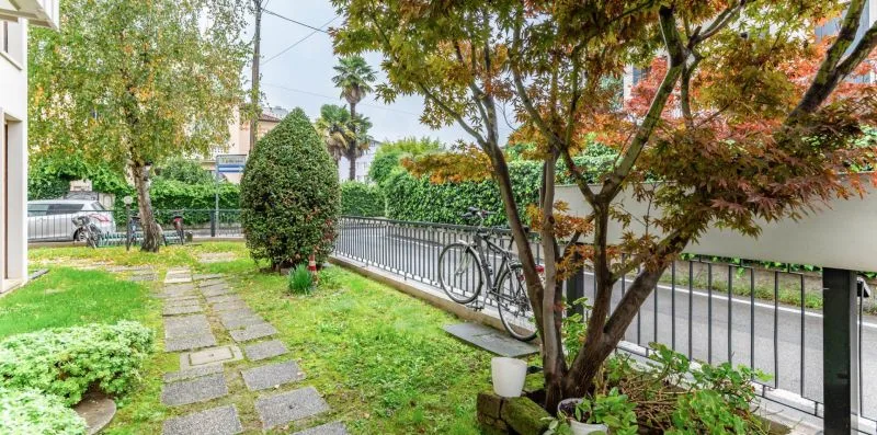 A garden path runs through a leafy outdoor courtyard beside a metal railing.