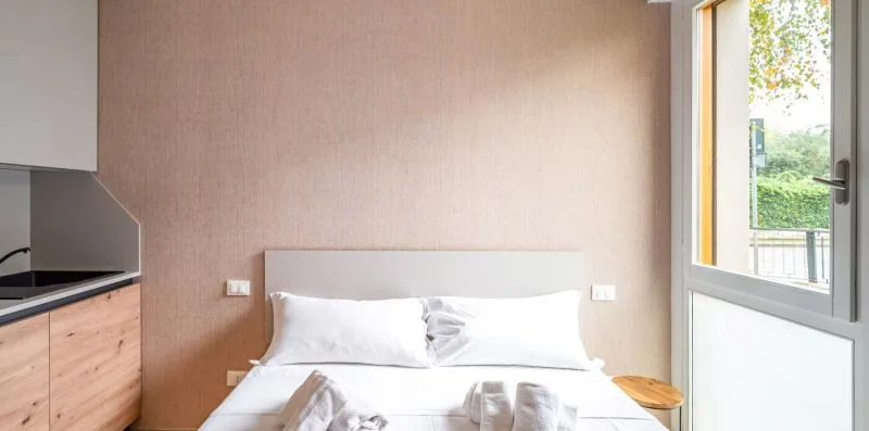 Un dormitorio con una cama junto a una ventana alta y una pequeña mesa de noche.