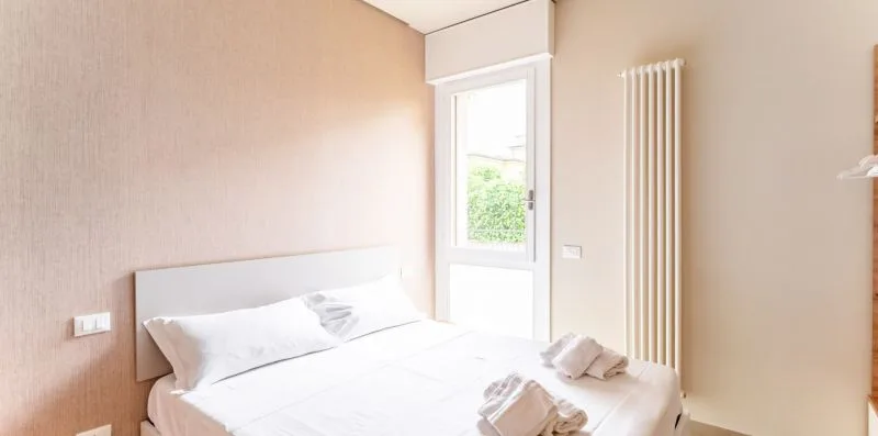 Un dormitorio luminoso con una cama blanca junto a una ventana alta.