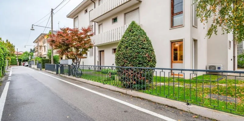 A residential street beside a white apartment building and landscaped garden.