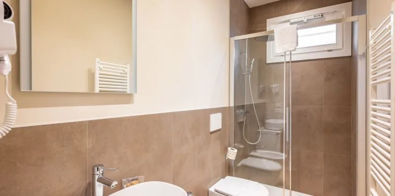 A bathroom with a glass shower, sink, and wall mirror.