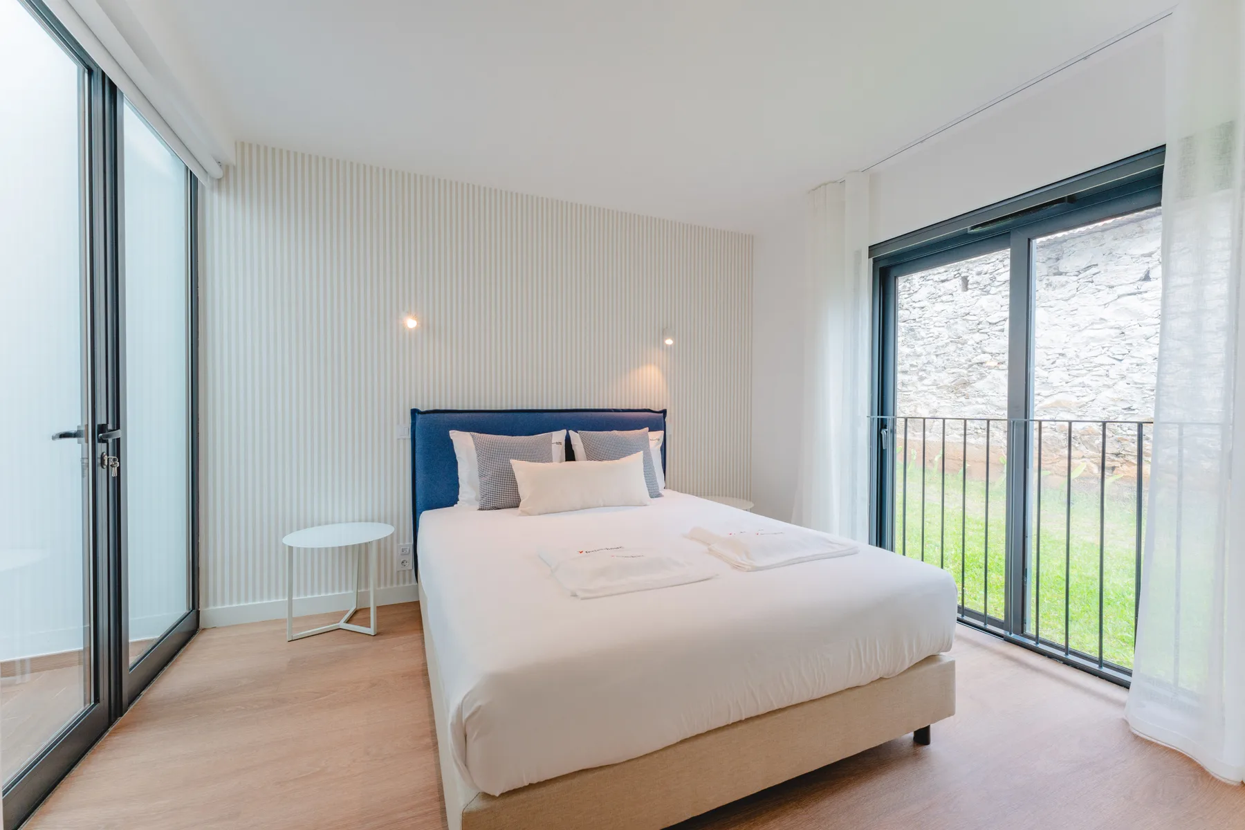 A bright bedroom with a neatly made bed beside large glass doors.