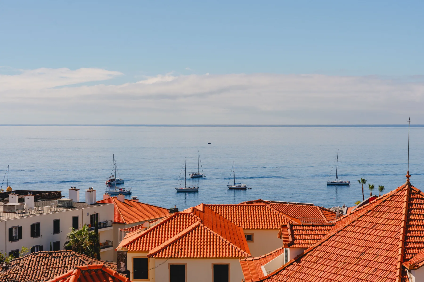 Red-tiled rooftops overlook the sea, with several boats visible on the water.