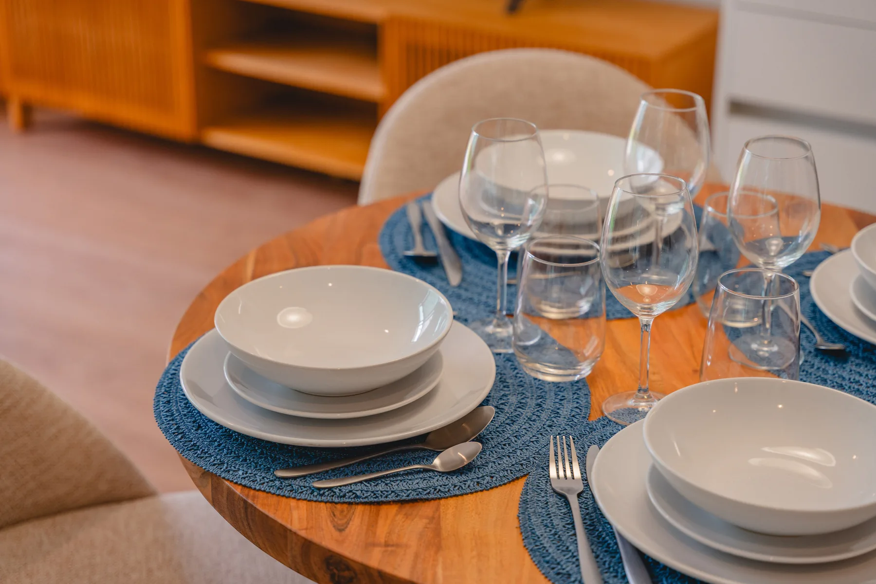 A dining table is set with white dishes, glasses, and blue placemats.