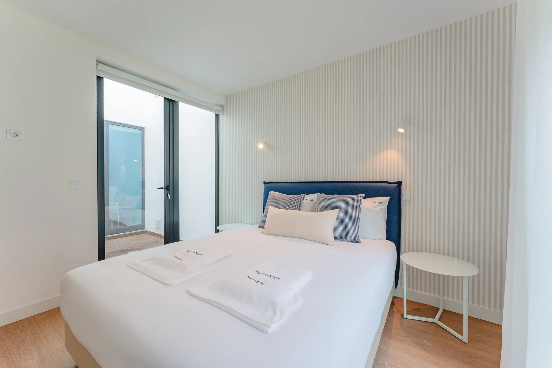 A bright bedroom with a neatly made bed beside a glass door.