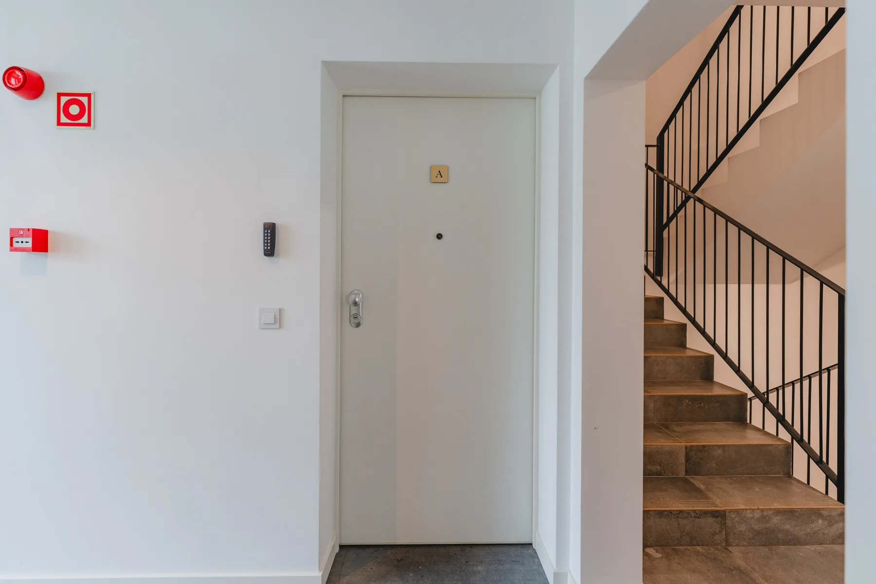 An interior hallway with a closed entrance door beside a staircase.