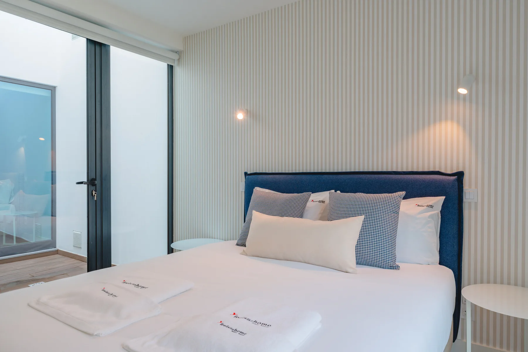 A bedroom with a neatly made bed beside a glass balcony door.