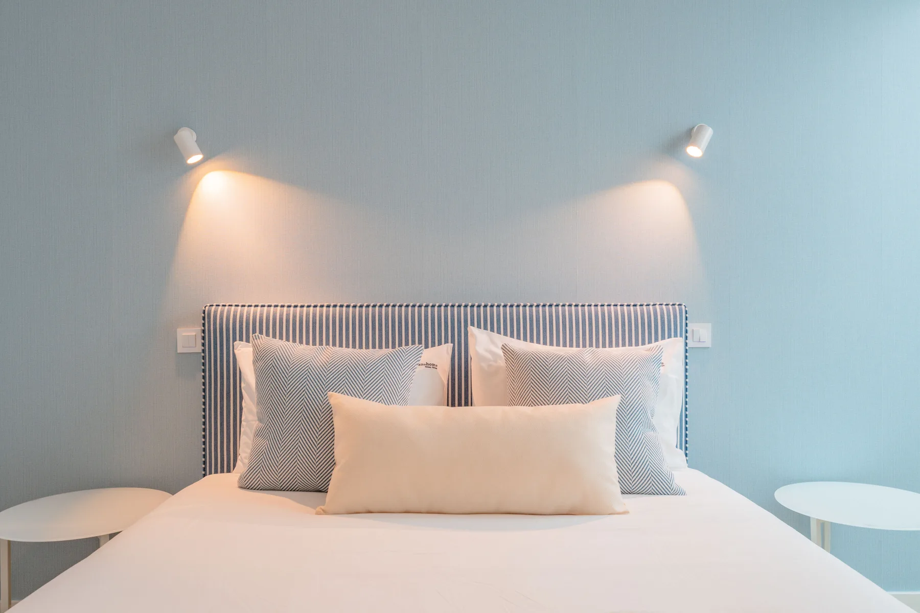A bedroom with a neatly made bed and two wall lights.