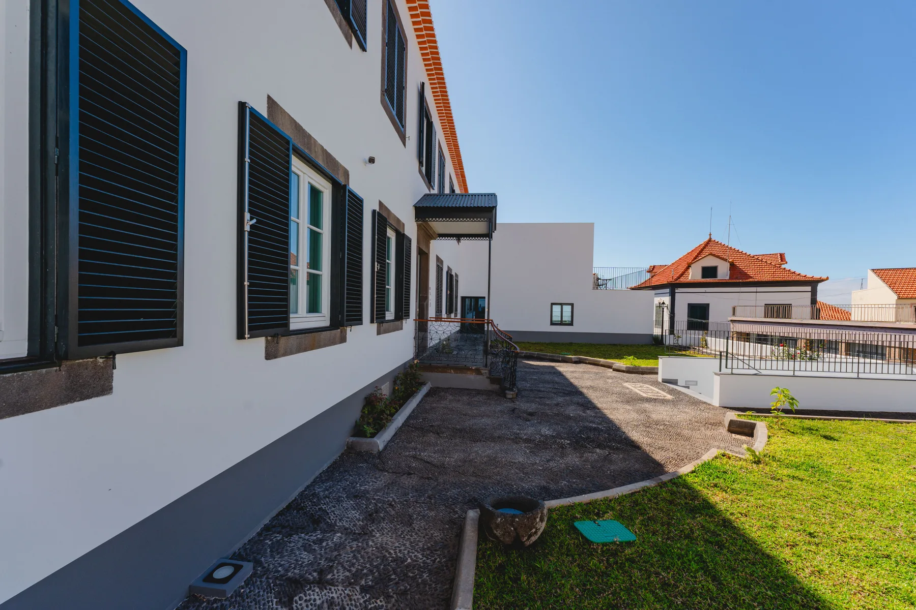 Exterior walkway beside a white building with shuttered windows and a grassy yard.