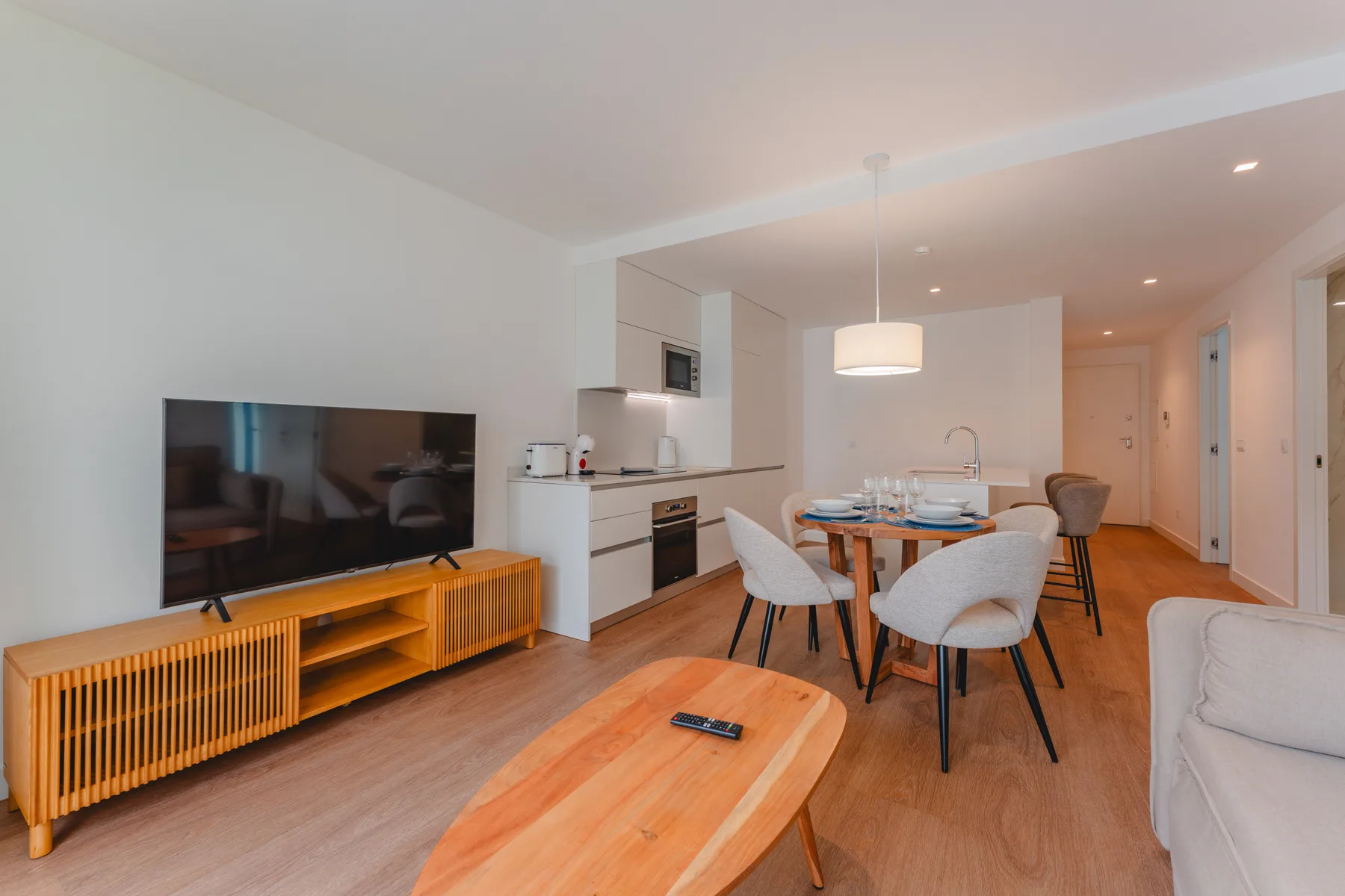 A bright living and dining area with a television, table, and kitchen.