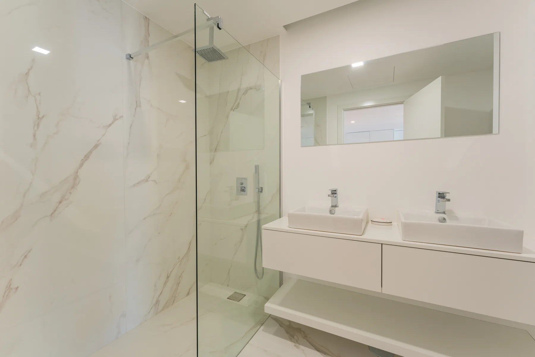 A bright bathroom with a glass shower and a double-sink vanity.