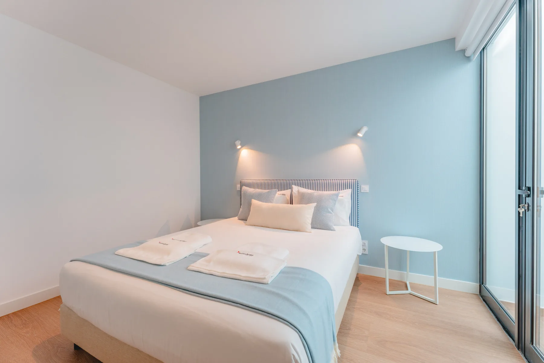 A bedroom with a bed, pale blue accent wall, and glass doors.