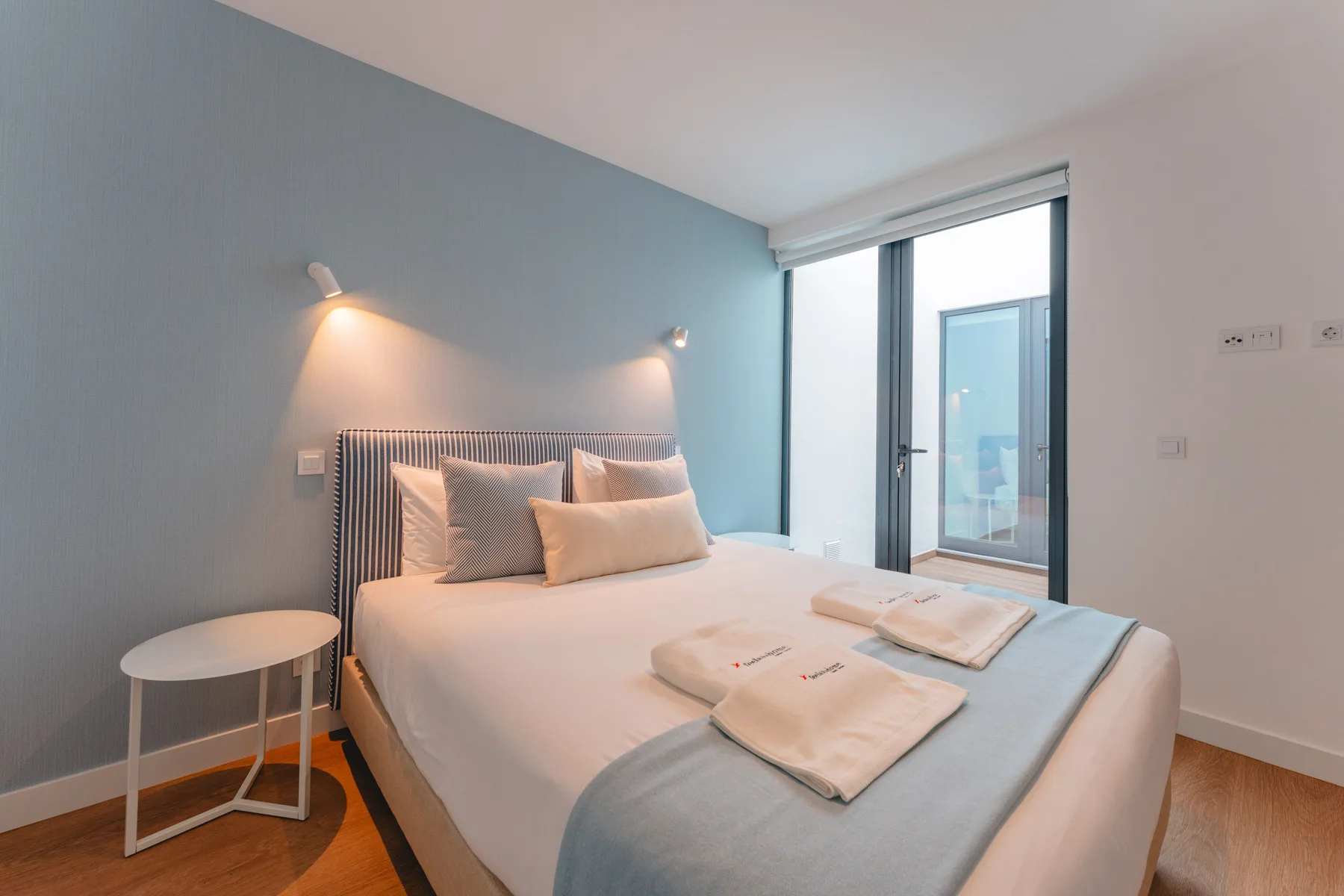 A bedroom with a neatly made bed and wall-mounted reading lights.