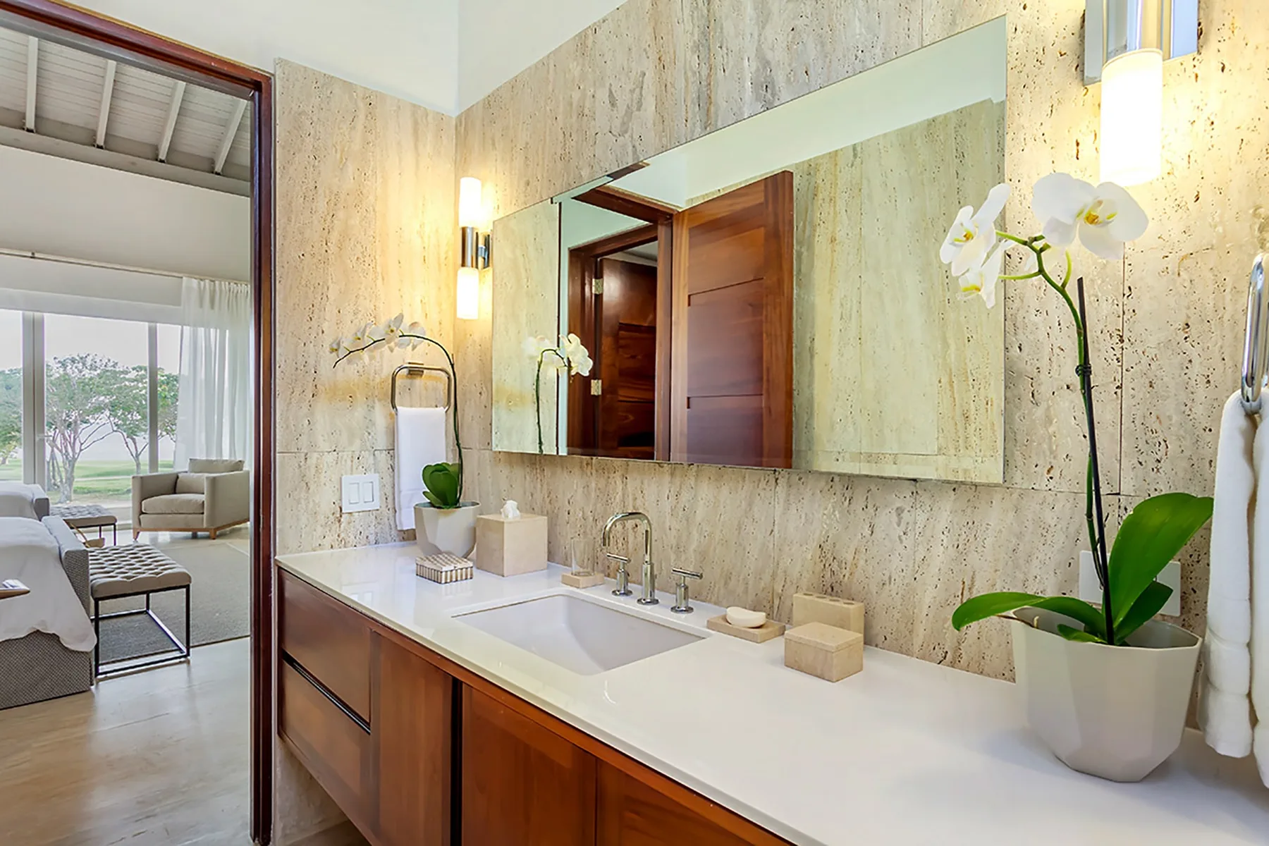 Un tocador de baño con una encimera larga, lavabo, espejo y orquídea en maceta.