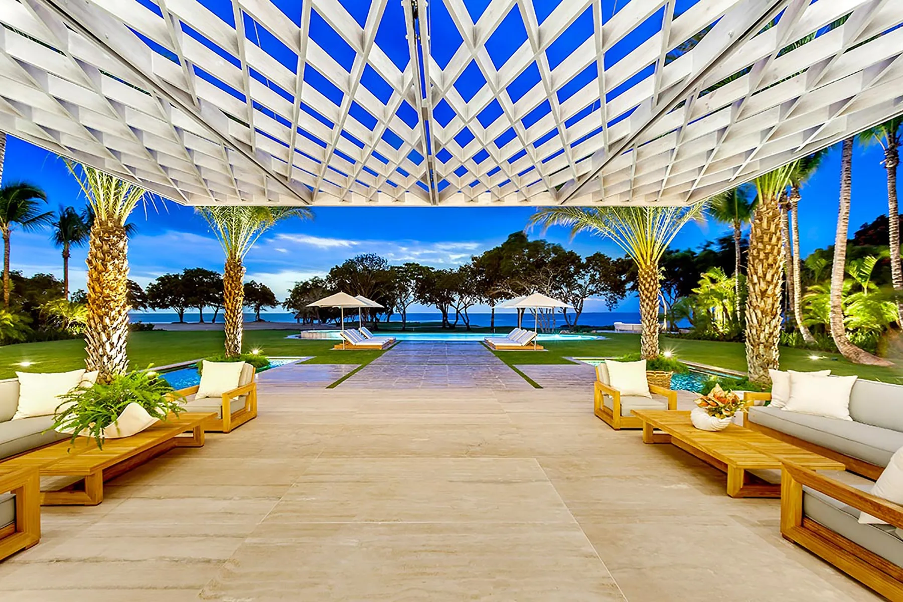 Una terraza lounge al aire libre da a una piscina y jardines con palmeras.