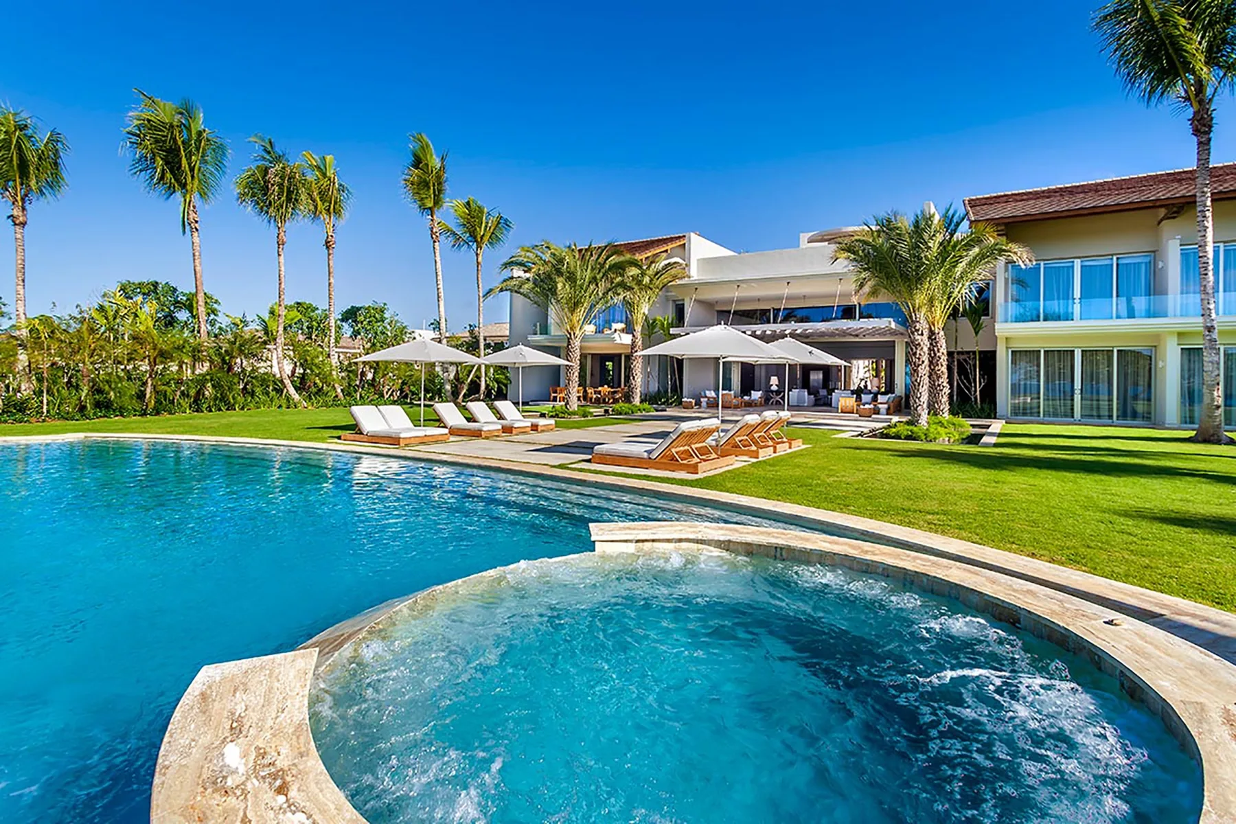 Una piscina y un spa circular junto a una casa moderna y palmeras.
