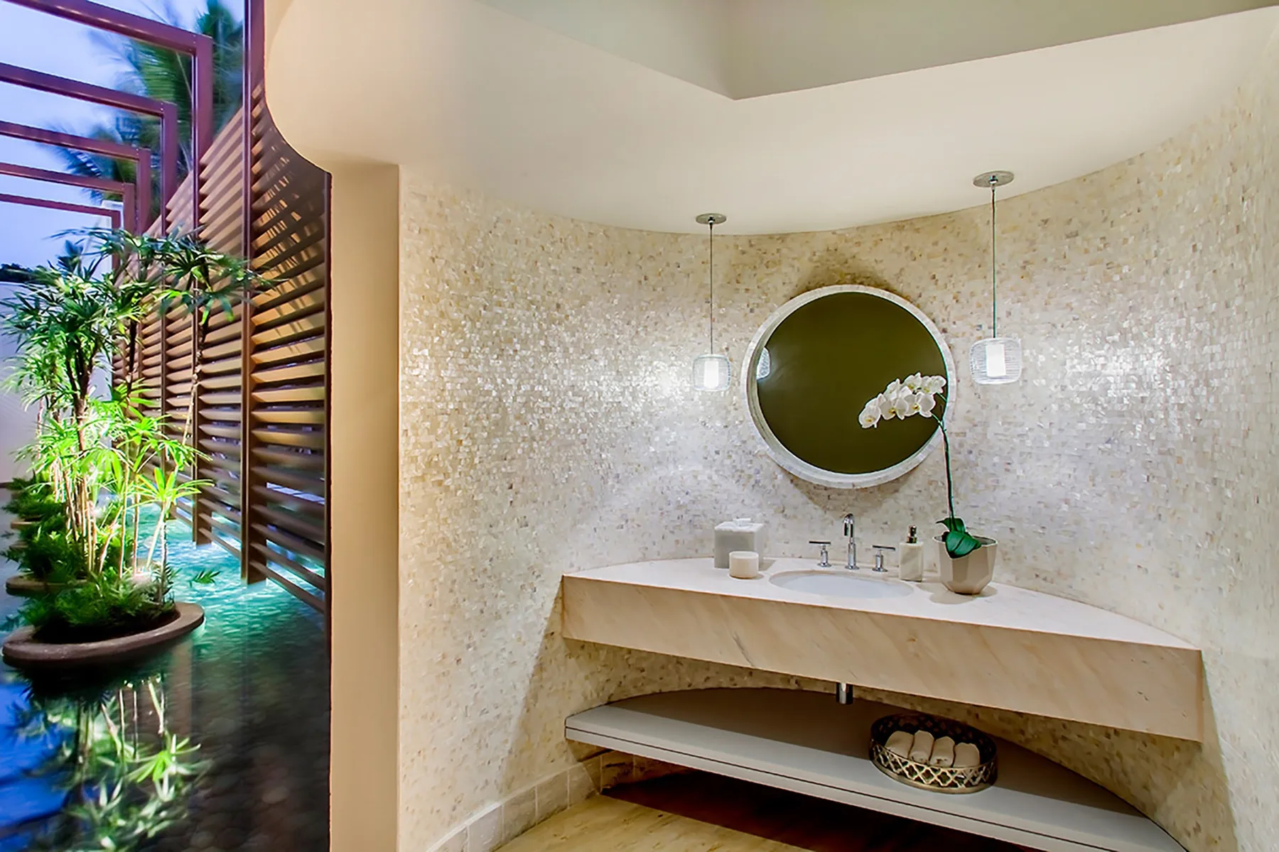 Un lavabo de baño con espejo redondo y una planta junto a un panel de listones.