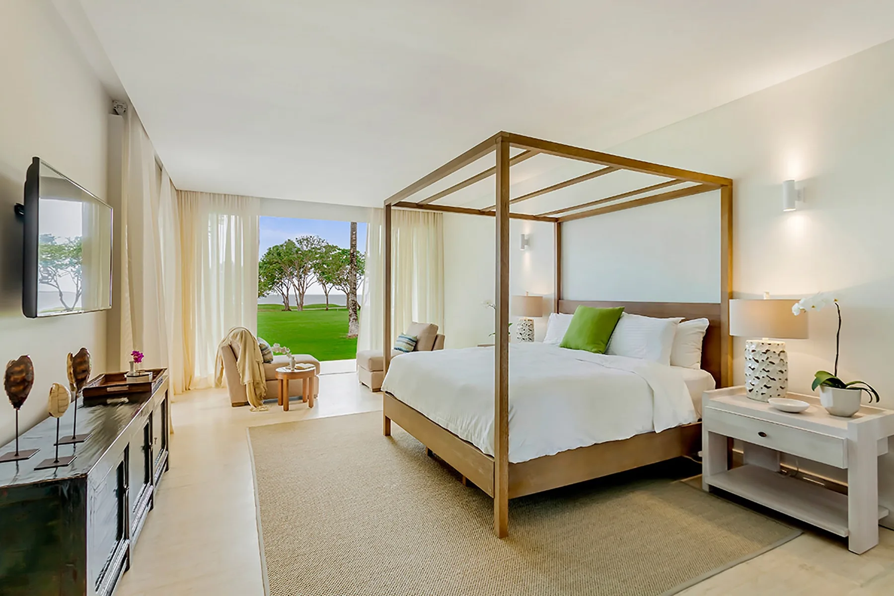 Un dormitorio luminoso con una cama con dosel y grandes ventanales con vistas a un césped verde.